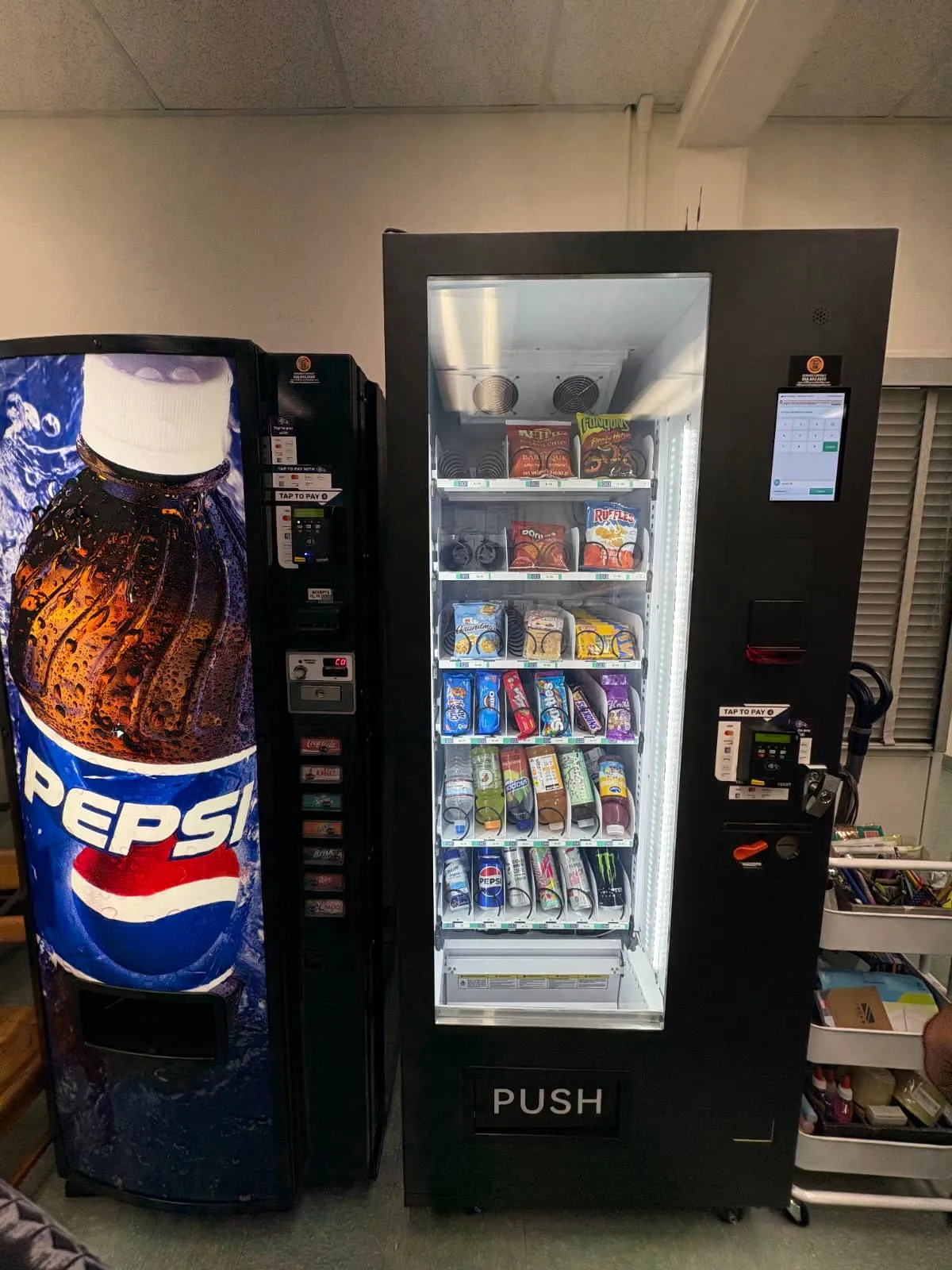 New glass-front combo vending machine with touchscreen installed in a staff breakroom next to a Pepsi machine